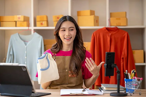 A seller at a desk filming her clothing rail on a phone tripod