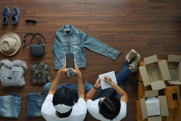 Two people packing folded denim and accessories into boxes, seen from above