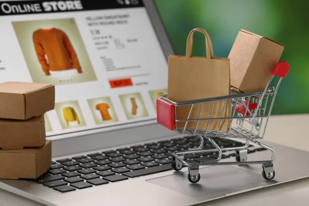 An online shop open on a laptop beside parcels and a shopping trolley