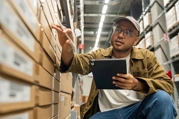 A worker checking stock on a tablet in a warehouse aisle